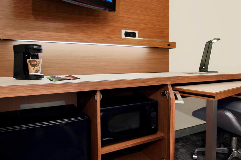 Hotel room desk with wood paneling, coffee maker, TV, and modern office setup