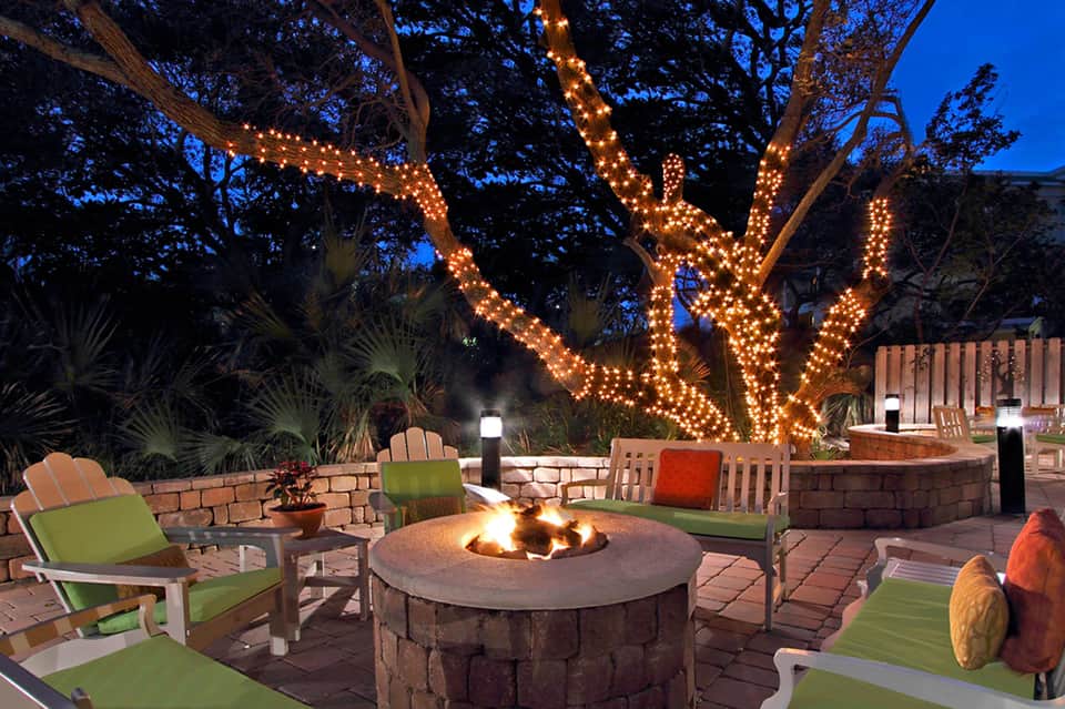 Fire pit area with illuminated trees, green cushioned seating, and stone surround