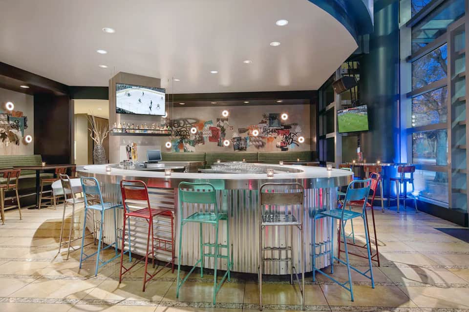 Modern hotel bar with colorful metal stools, backlit shelving, and contemporary design elements