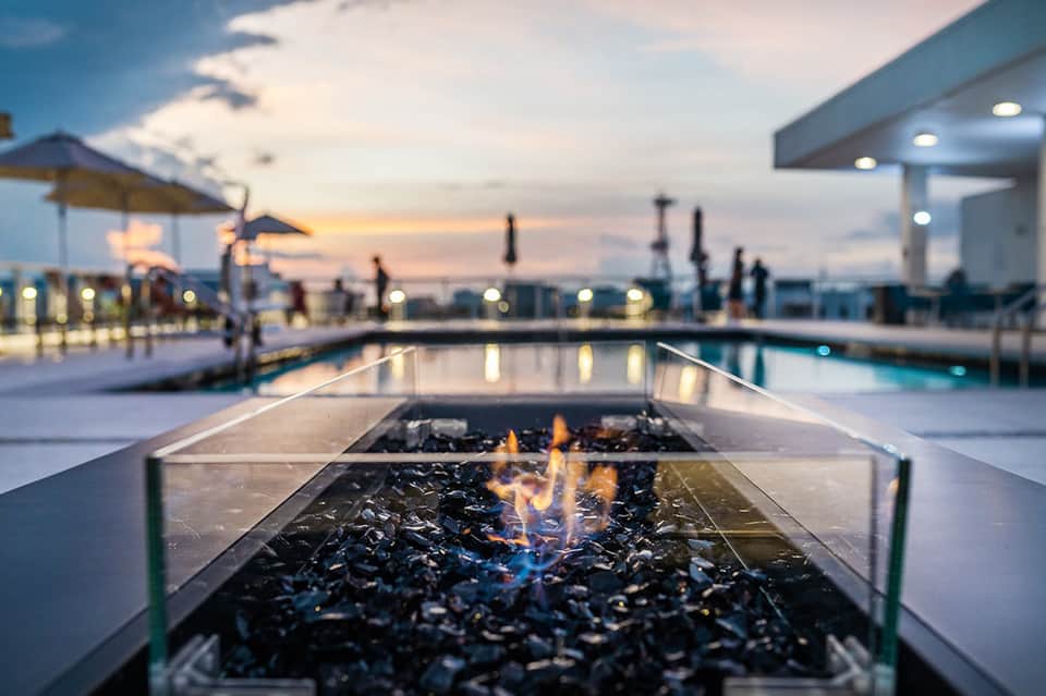 Modern firepit at resort deck at dusk with pool and landscape lighting reflecting on water