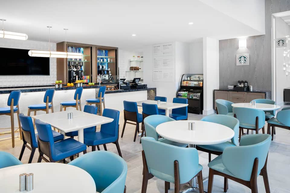 Modern hotel coffee bar and lounge with blue chairs, white tables, and contemporary decor