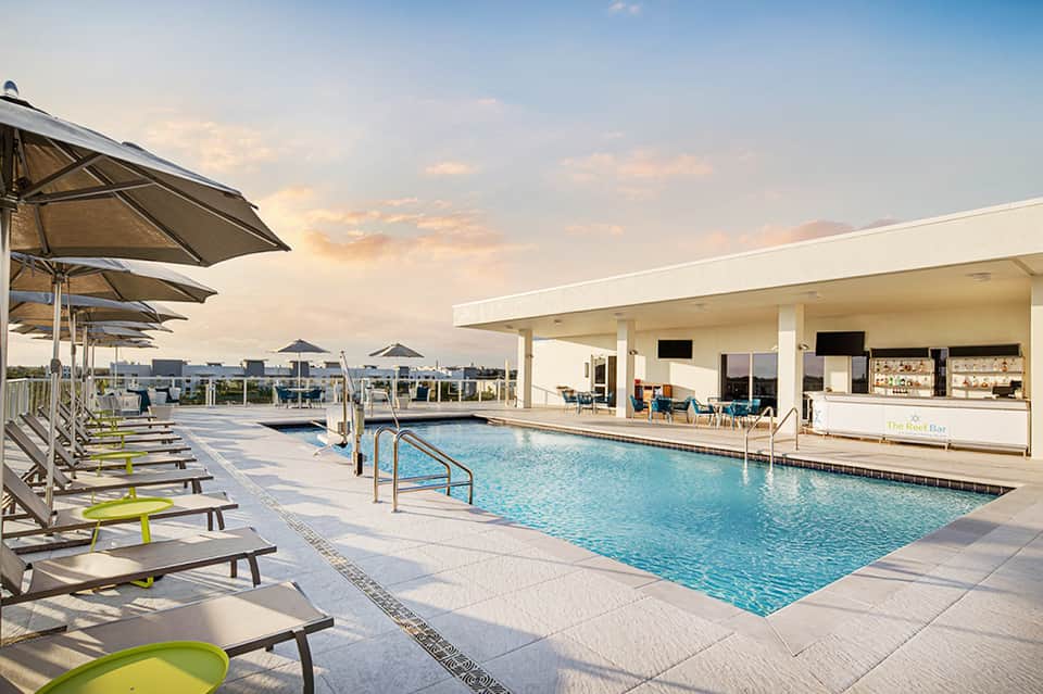 Contemporary pool area at dusk with lounge chairs, umbrellas, and bar pavilion