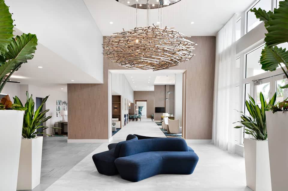 Modern hotel lobby with artistic branch chandelier, blue curved sofa, potted plants, and natural light