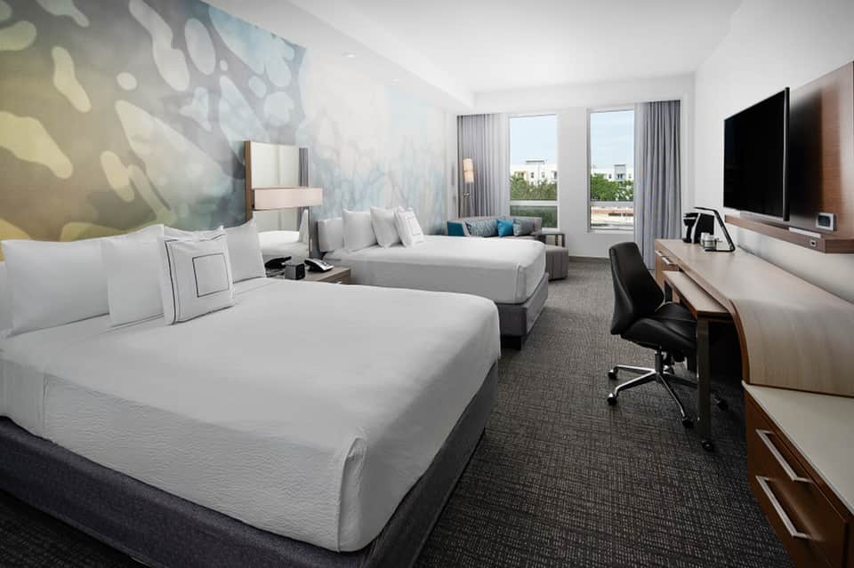 Hotel guest room with dual queen beds, flat-screen TV, work desk, and patterned accent wall art