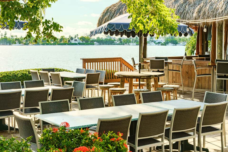 Waterfront patio with dining tables, thatched umbrellas, decorative elements, and canal or lagoon view