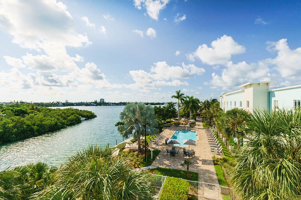 Aerial view of beachfront resort pool with palm trees and waterway landscape