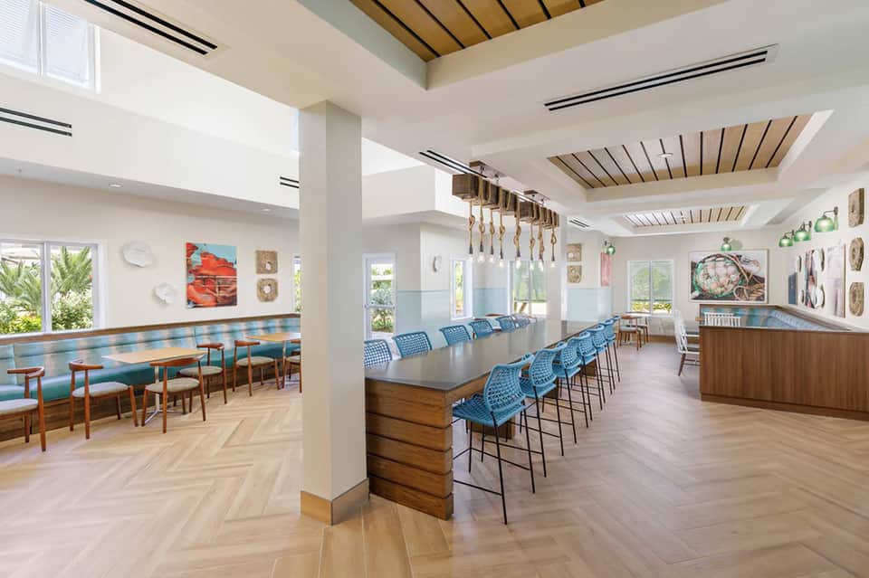 Modern cafeteria with wooden ceiling beams, long communal tables, and coastal artwork