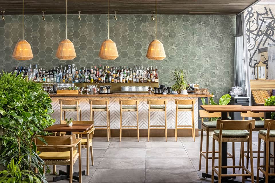 Elegant bar lounge with wooden herringbone bar front, four woven pendant lights, hexagonal tile walls, and wooden chairs