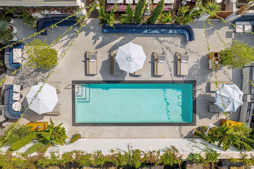 Aerial view of rectangular pool with loungers, umbrellas, and surrounding landscaping