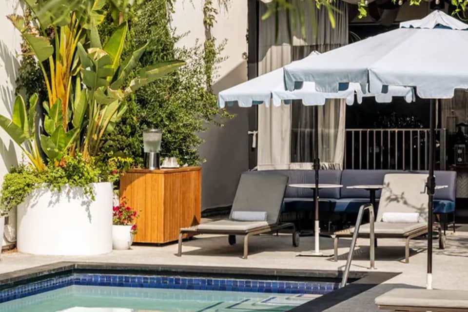 Resort pool deck with lounge chairs, white umbrella, and lush landscaping
