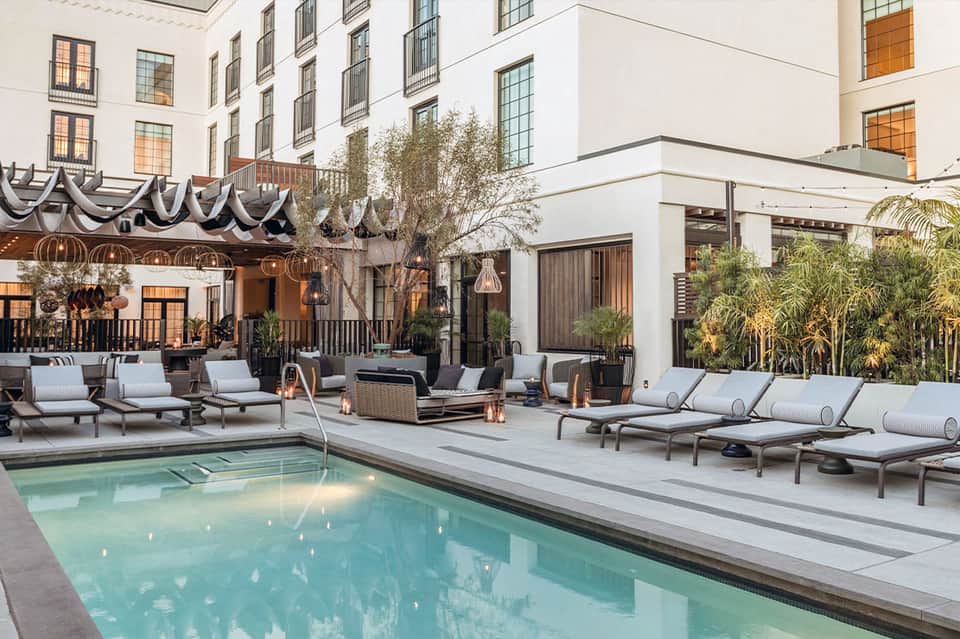 Upscale courtyard pool with scalloped awning, loungers, palms, and contemporary hotel building facade
