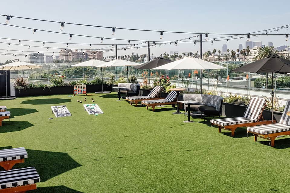 Rooftop lounge with artificial turf, string lights, lounge chairs, and city views