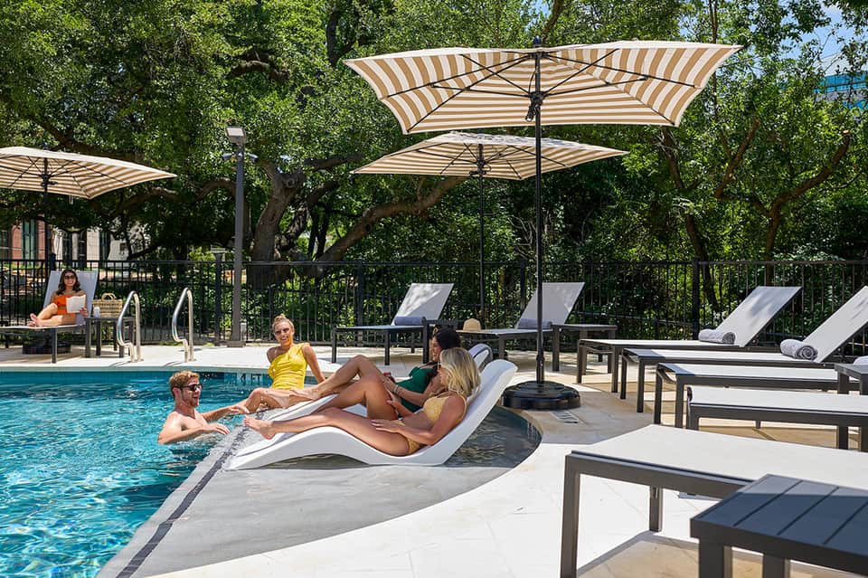 Outdoor pool with striped umbrellas, modern lounge chairs, and shaded seating areas surrounded by trees