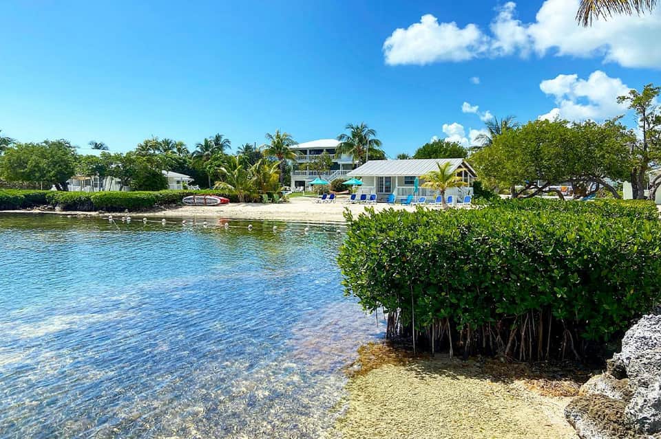 Waterfront homes with white buildings, beach, mangrove vegetation, and clear turquoise water