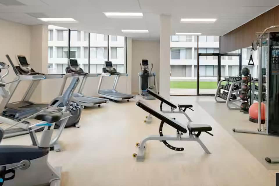 Modern fitness center with treadmills, exercise bikes, and large windows overlooking grounds