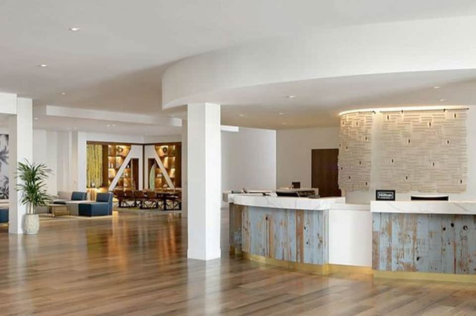 Modern hotel lobby with polished wood floors, white columns, and rustic wood reception desk