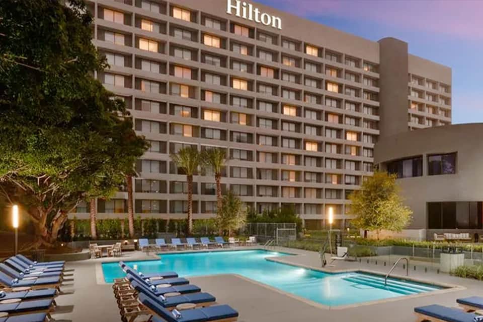 Hilton hotel twilight pool scene with illuminated high-rise building, loungers, and landscaped grounds