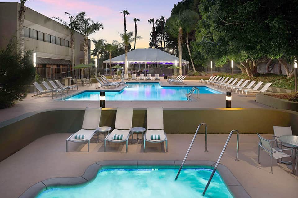 Resort pool at dusk with tent pavilion, lounge chairs, palm trees, and illuminated spa area