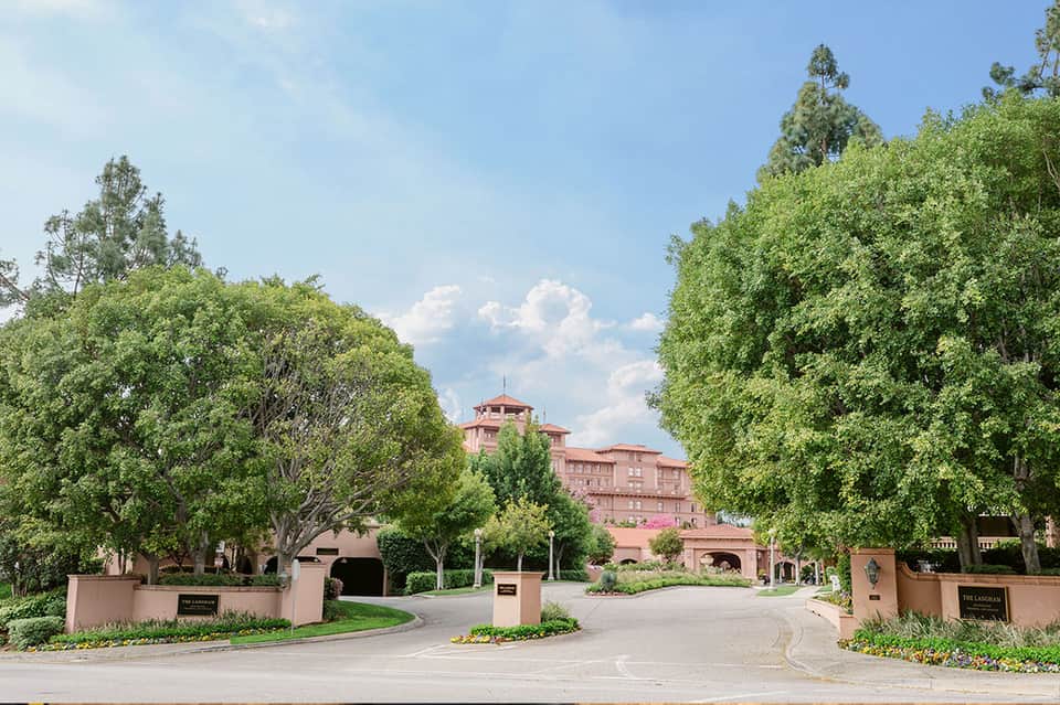 Tree-lined driveway entrance to pink Mediterranean-style mansion with manicured grounds