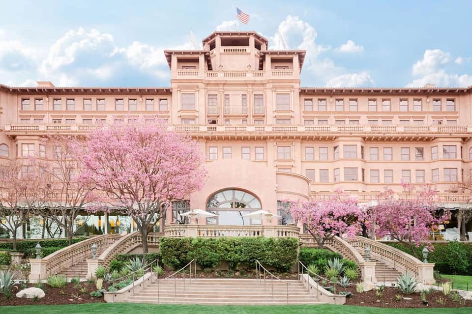 Historic pink neoclassical building with blooming pink trees and fountain in foreground