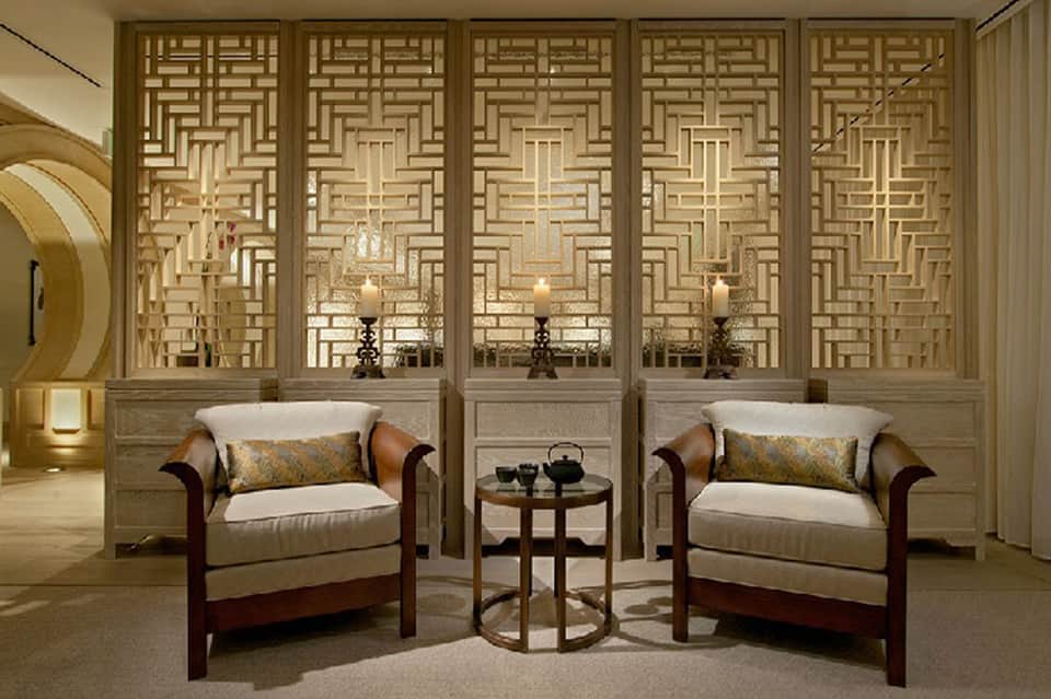 Luxe sitting room with geometric wooden screens, cream armchairs, and side table