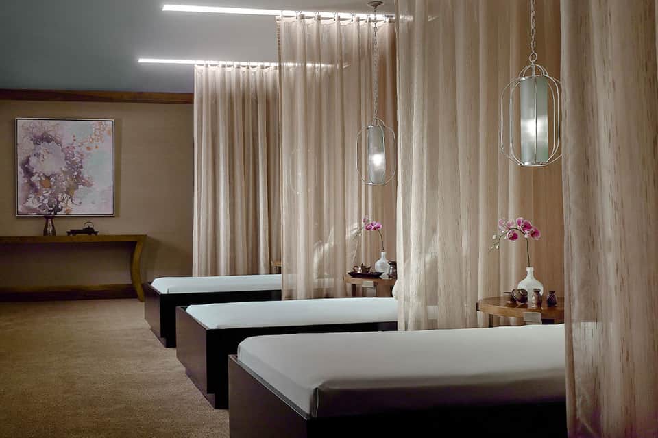 Spa treatment room with massage beds, hanging pendant lights, and pink orchid flowers