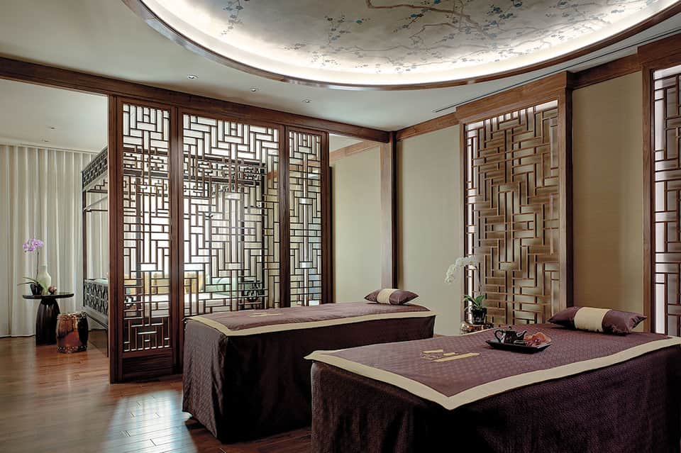 Luxury spa treatment room with twin massage beds and decorative wood screens