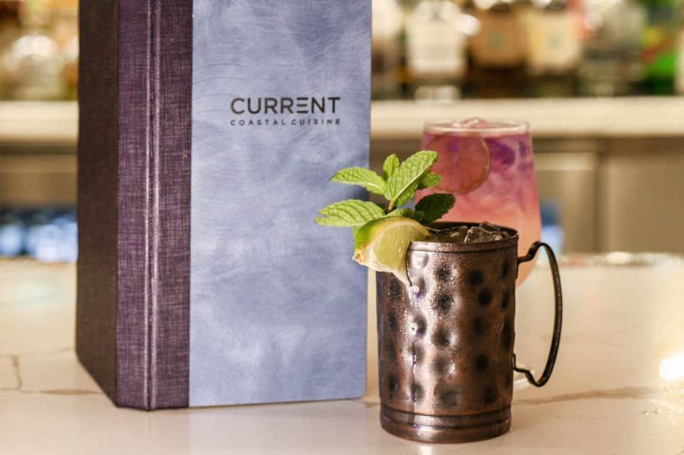 Metallic Moscow mule cocktail with lime and mint next to Current restaurant menu