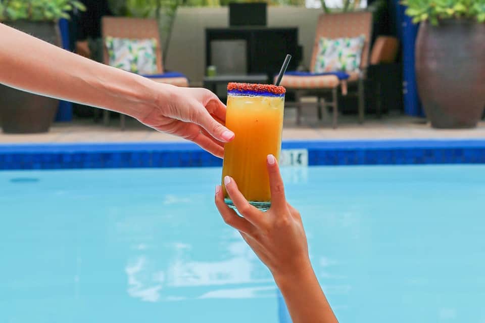 Colorful cocktail with blue and orange rim held over resort swimming pool at daytime