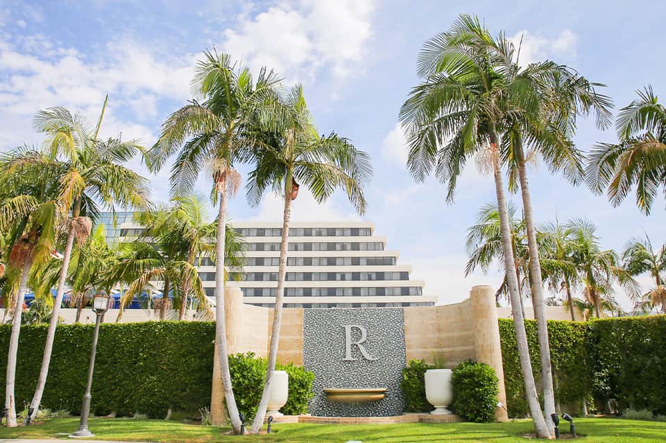 Resort entrance with tall palm trees and modern multi-story building behind stone wall