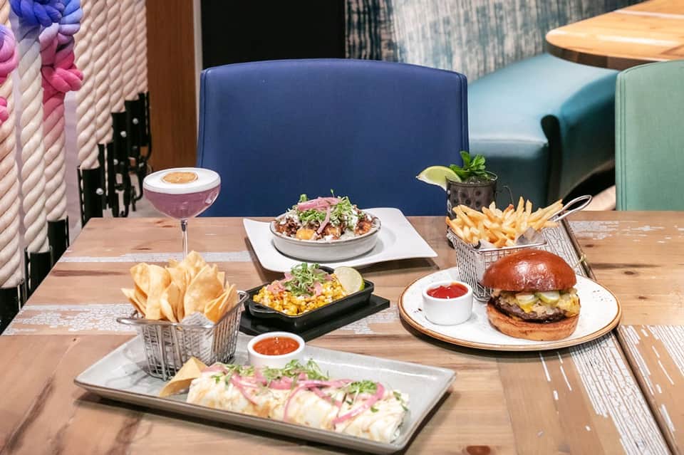 Contemporary restaurant table with cocktail, burger, fries, and appetizers with colorful seating