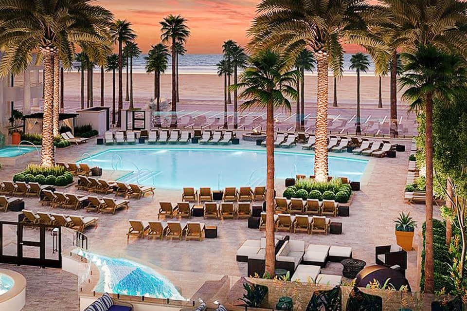Beachfront resort pool at sunset with palm trees, lounge chairs, and ocean view