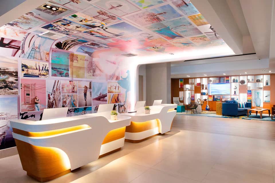 Contemporary hotel lobby with curved white reception desk, colorful ceiling art, and vibrant furnishings