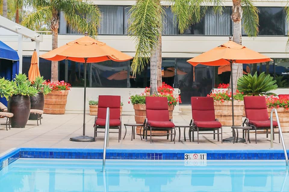 Resort poolside seating area with orange umbrellas, red lounge chairs, and palm trees