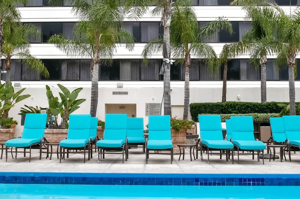 Hotel poolside with turquoise lounge chairs, palm trees, and white building facade