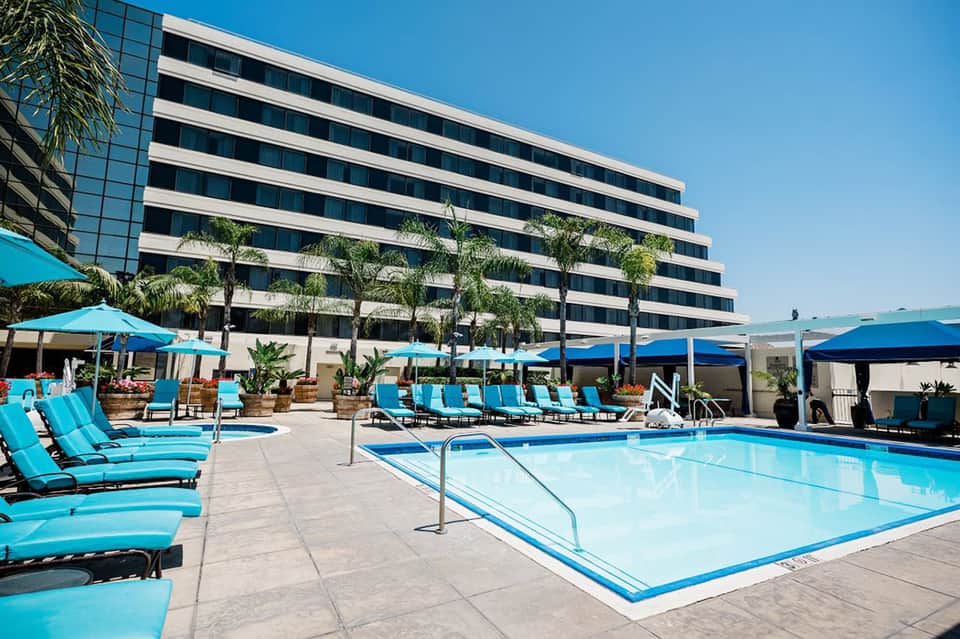 Modern resort pool deck with turquoise umbrellas, lounge chairs, and high-rise building