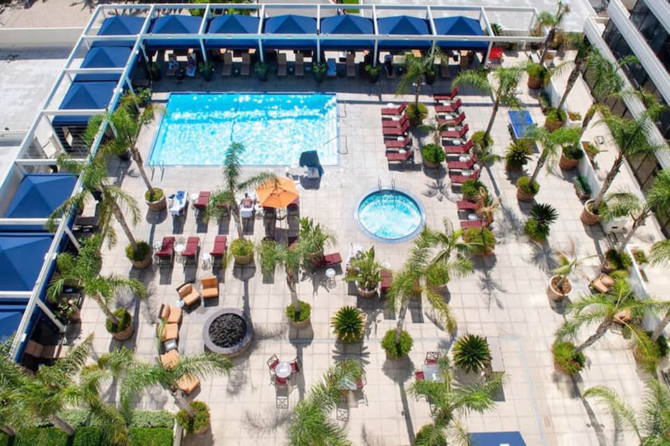 Aerial view of resort pool complex with red lounge chairs, umbrellas, and tropical landscaping