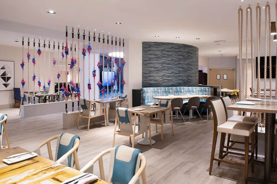 Modern hotel restaurant interior with wooden furniture, decorative hanging flowers, and water feature