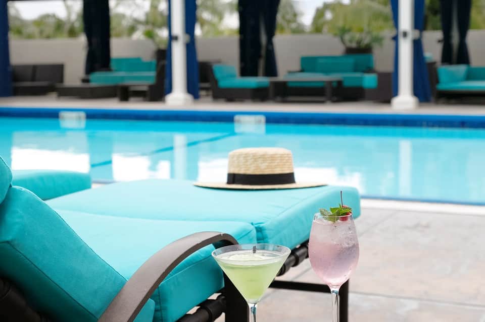 Poolside lounge chairs with cocktails, straw hat, and resort in background