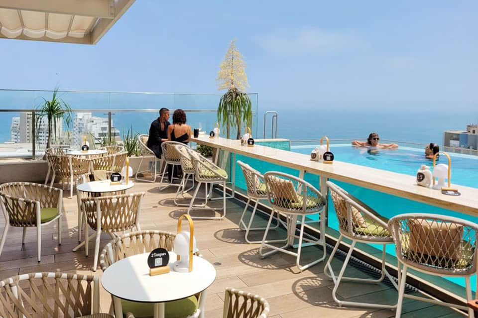 Upscale rooftop pool bar overlooking turquoise water and ocean coastline with woven chairs