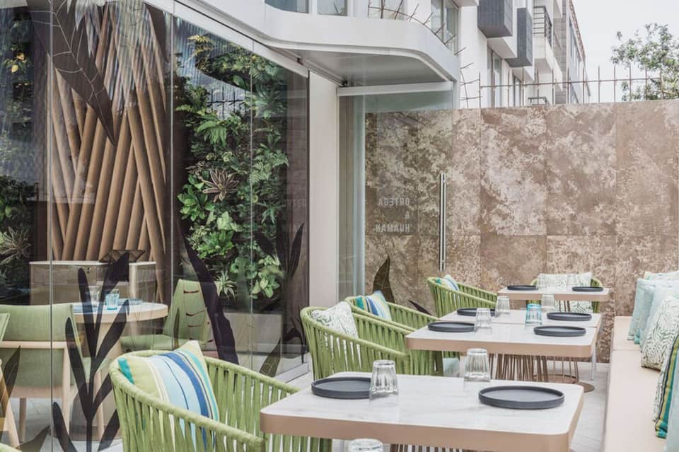 Modern restaurant terrace with green rope chairs, white tables, and living plant wall backdrop
