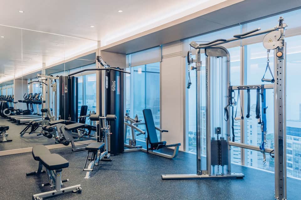 High-rise fitness center with cardio equipment and floor-to-ceiling windows overlooking ocean