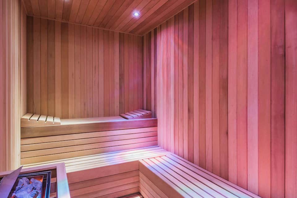 Modern sauna interior with light wood paneling and pink ambient lighting on the walls.