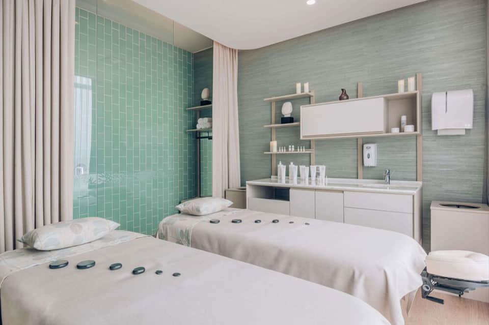 Spa treatment room with twin massage beds and green tile shower area with modern amenities