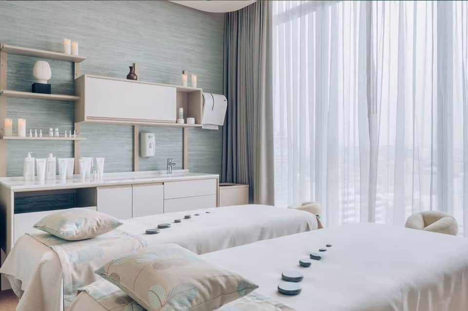Modern spa treatment room with twin beds, mint green walls, white storage, and ocean view