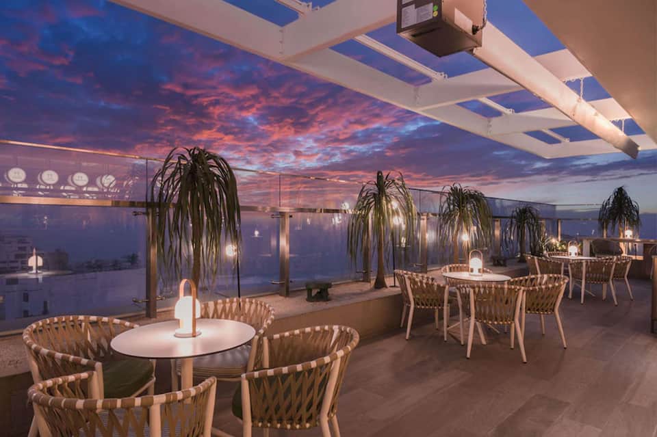 Rooftop restaurant terrace at twilight with draped seating, hanging plants, and panoramic water views