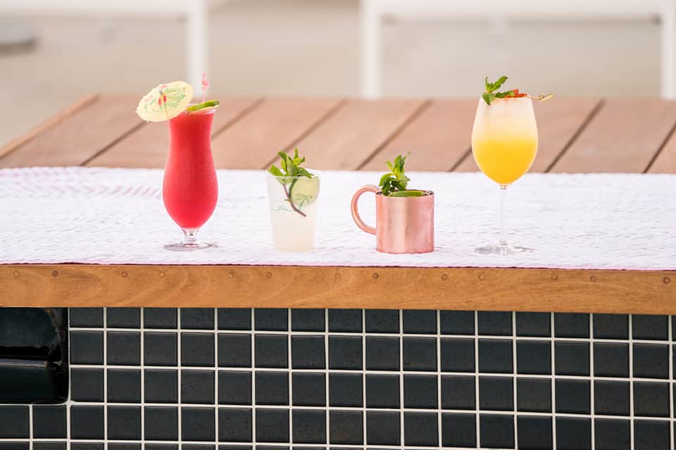 Colorful cocktails on poolside table with umbrellas and garnishes