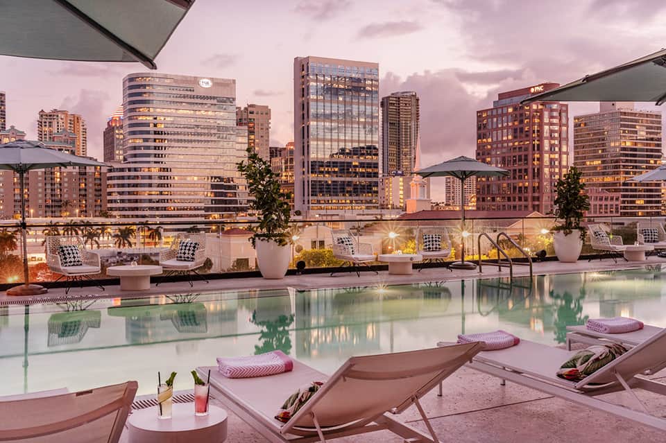 Urban rooftop pool at dusk with city skyline backdrop, lounge chairs, and modern furniture