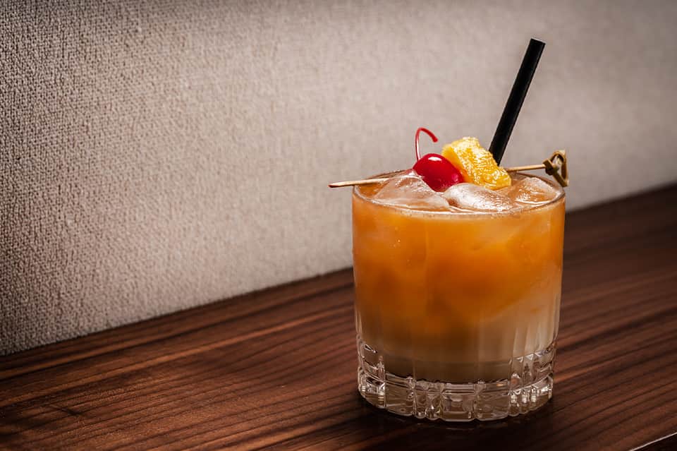 Craft cocktail with orange slice and cherry garnish on wooden table