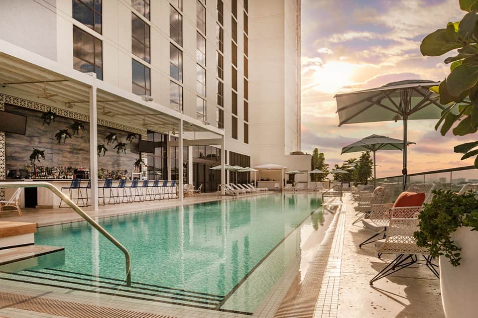 Modern hotel rooftop pool with turquoise water, lounge chairs, umbrellas, and sunset view
